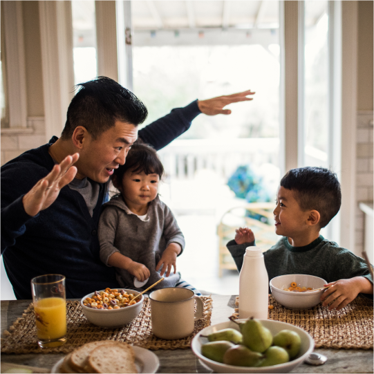 A dad entertains his two sons with a story while sitting around the breakfast table.