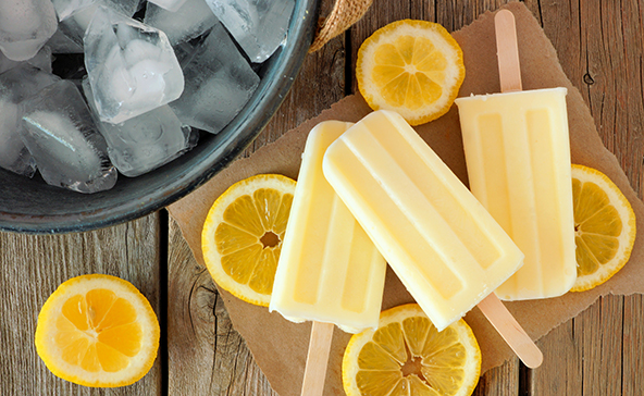 Three frozen lemon popsicles on a table with lemon slices surrounding them