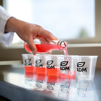 A hand pouring red liquid into ADM-branded cups 