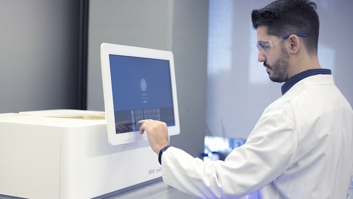 A scientist in a white coat analyses samples on a computer screen