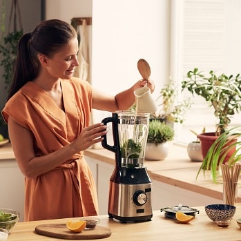 A young woman in a kitchen uses a blender