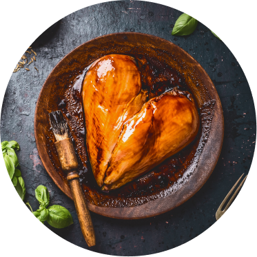 Two chicken breasts basted with a barbecue sauce are placed in a wooden bowl to form a heart