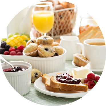 A continental breakfast spread with toast and jam, mini muffins, fruit, tea, and orange juice